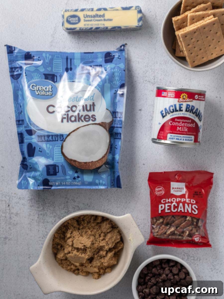 Golden Coconut Dream Bars 4 Top-down view of all the ingredients for magic bars laid out on a surface, including butter, brown sugar, graham crackers, condensed milk, chocolate chips, pecans, and shredded coconut.