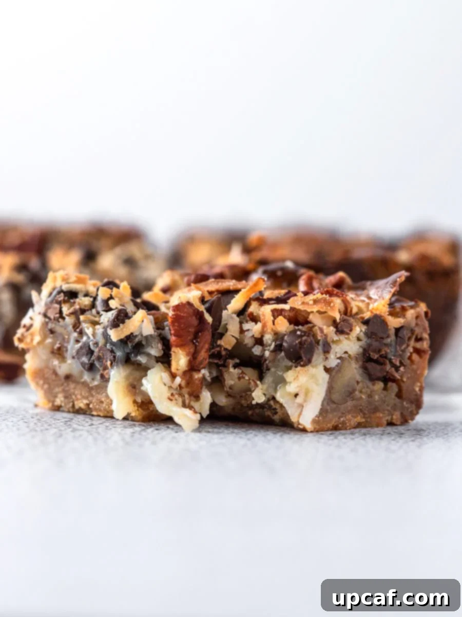 Golden Coconut Dream Bars 7 Side view of a coconut magic bar with a bite taken out, revealing the distinct chewy and gooey layers inside.