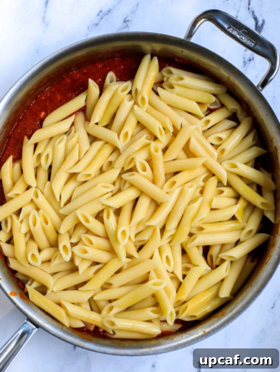 Raging Inferno Pasta 10 Cooked pasta being added to the tomato sauce in a pot.