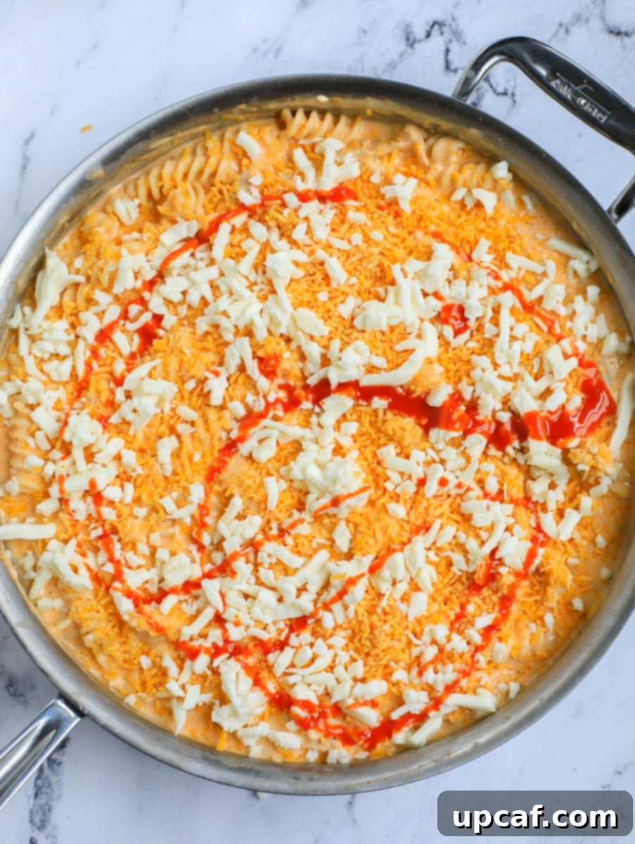 Fiery Buffalo Chicken Pasta Bake 12 Buffalo sauce and cheese on top of pasta in a pot, ready for baking.