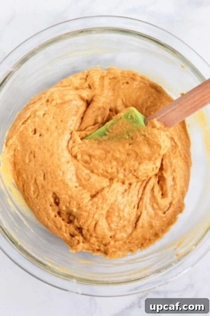 Top down shot of a spatula mixing pumpkin bread batter in a glass bowl.