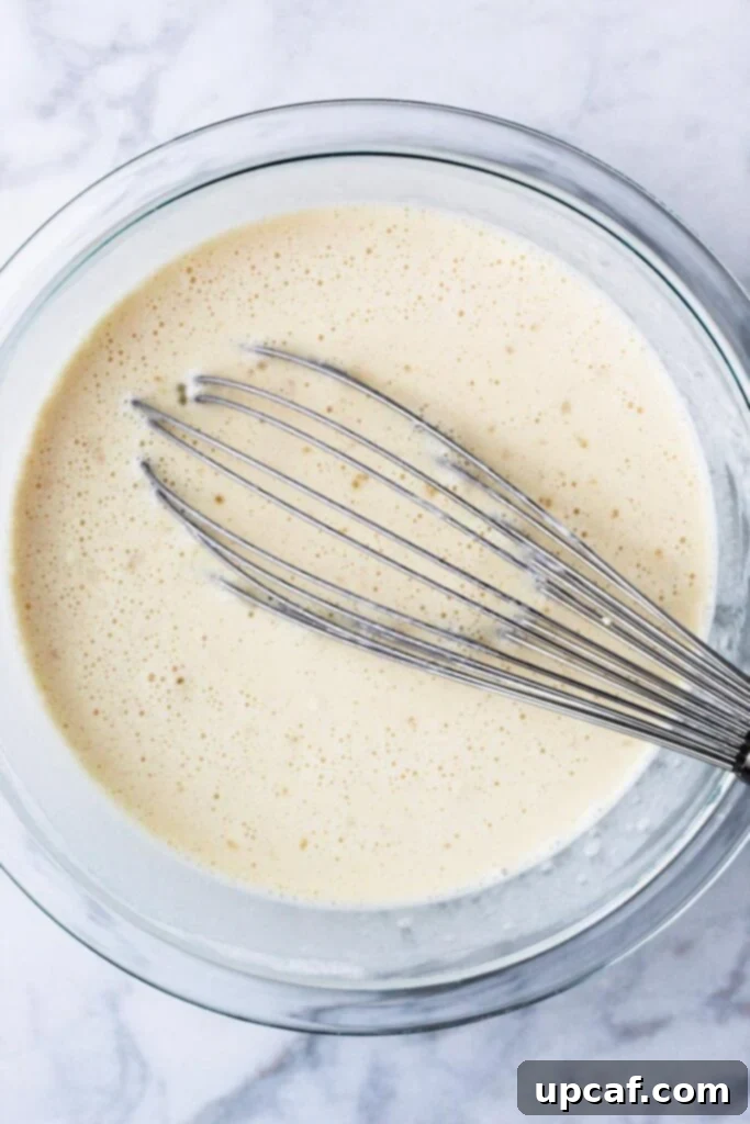 A whisk being used to mix crepe batter in a large bowl, illustrating the smooth, lump-free consistency needed.