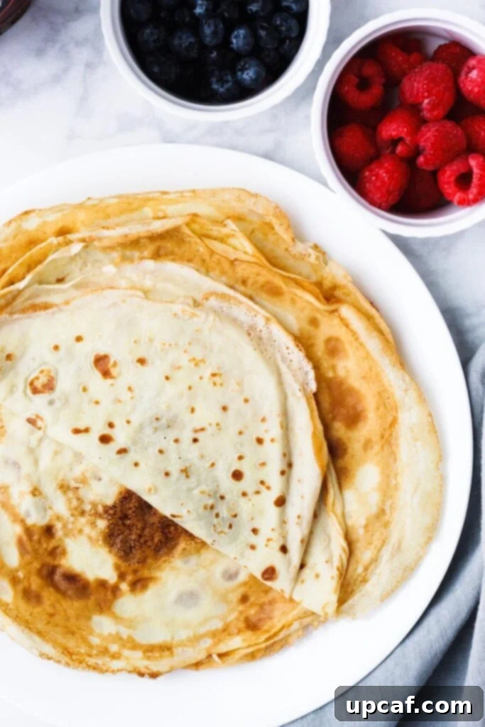A beautiful stack of perfectly cooked, golden crepes arranged on a white plate, ready for delicious fillings.