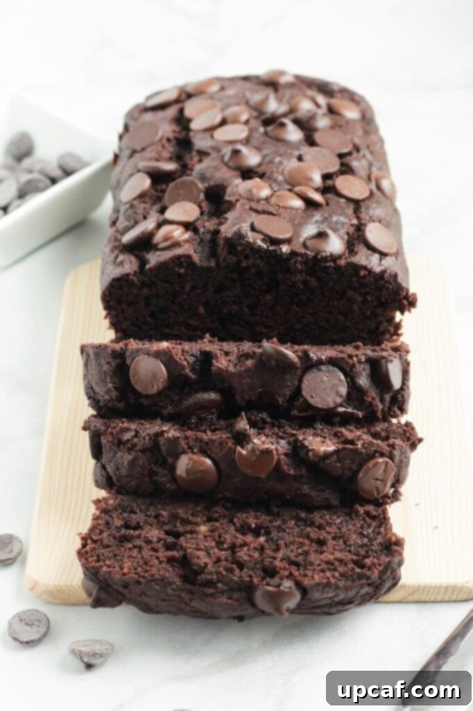 Sliced chocolate banana bread on a rustic wooden board, showing its moist texture and abundant chocolate chips within.