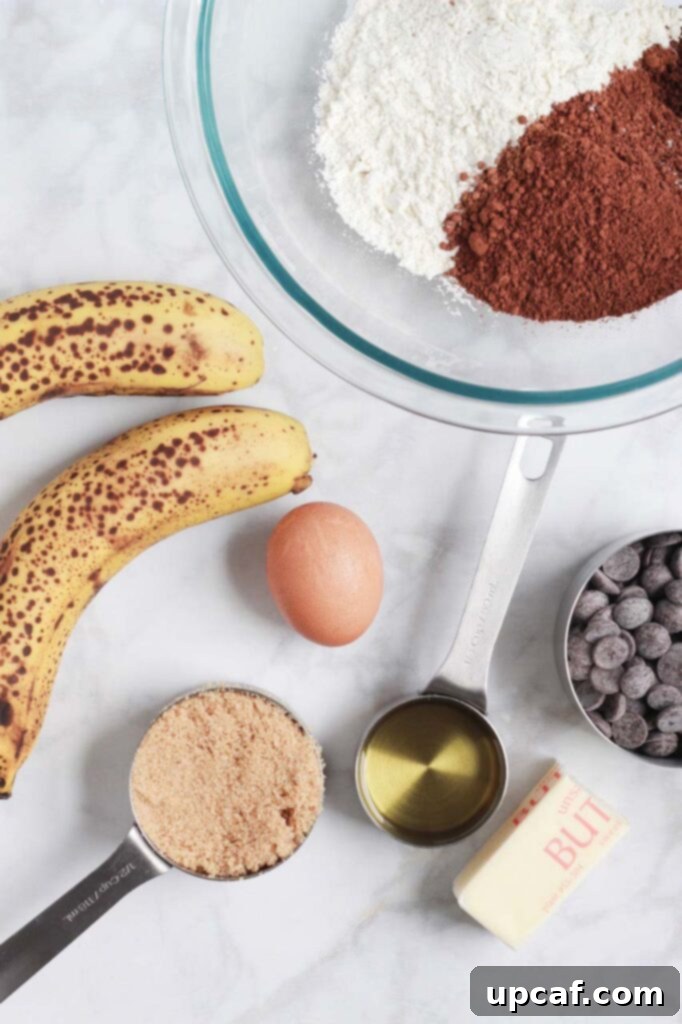 Assortment of fresh ingredients laid out for making chocolate banana bread, including bananas, flour, cocoa powder, and chocolate chips.