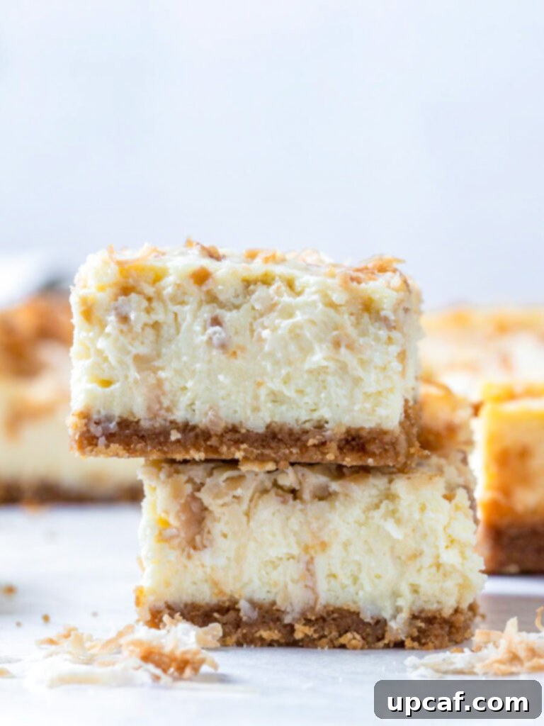 Stacked coconut cheesecake bars on a pristine white plate, showcasing their creamy texture and golden toasted coconut topping