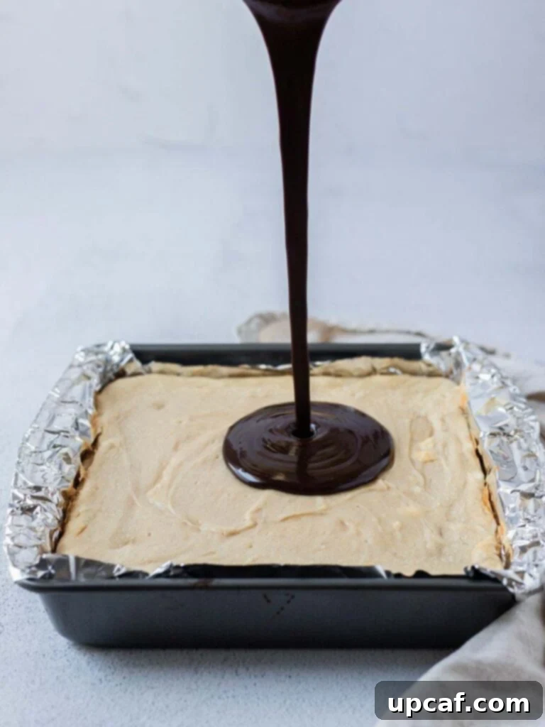 A close-up shot of rich, glossy chocolate ganache being poured evenly over a golden-brown peanut butter cheesecake, still in its baking pan.