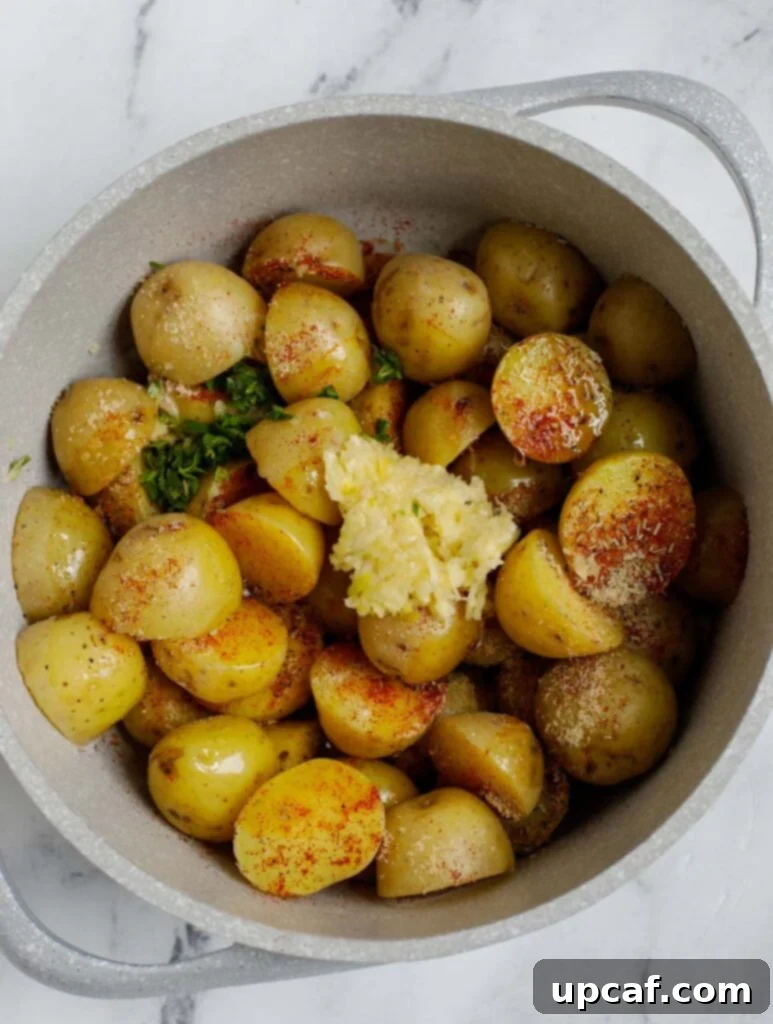 Top down shot of potatoes being mixed with herbs, garlic, and olive oil in a white bowl.