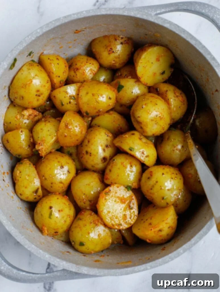 Potatoes covered in olive oil being mixed with a spoon in a white bowl, showing the coating process.