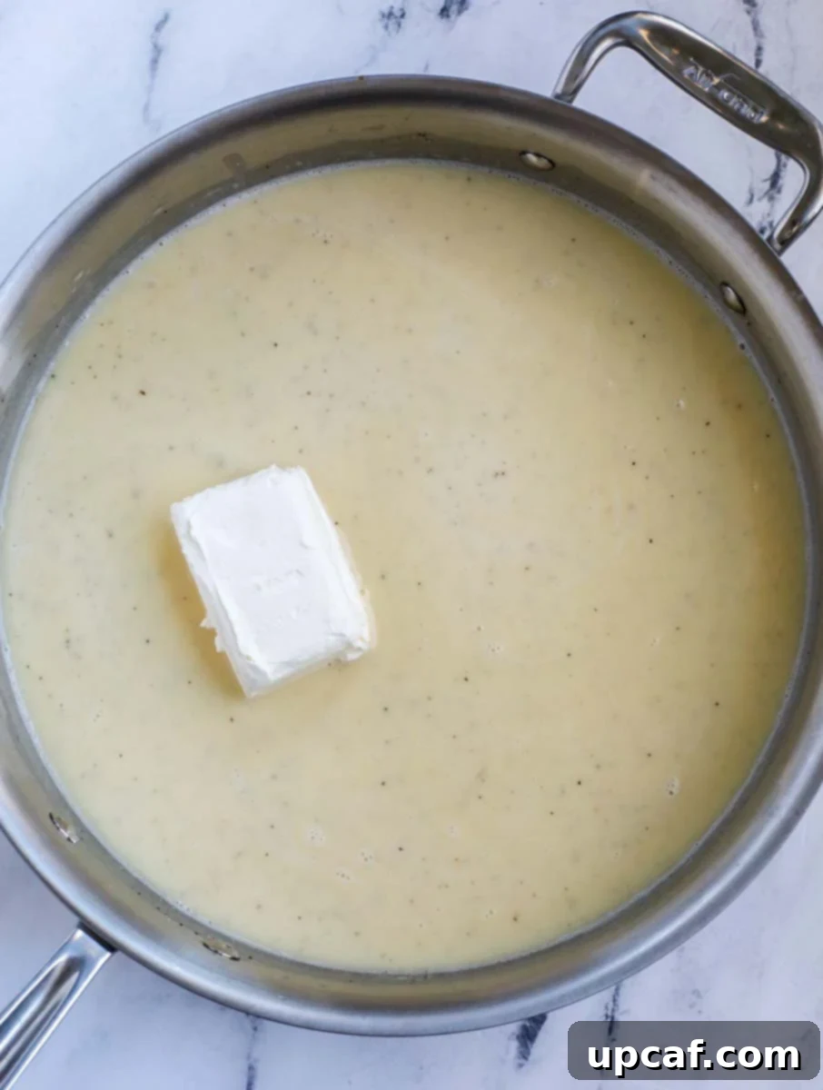 A stainless steel skillet containing a creamy casserole sauce base with a block of cream cheese melting into it.