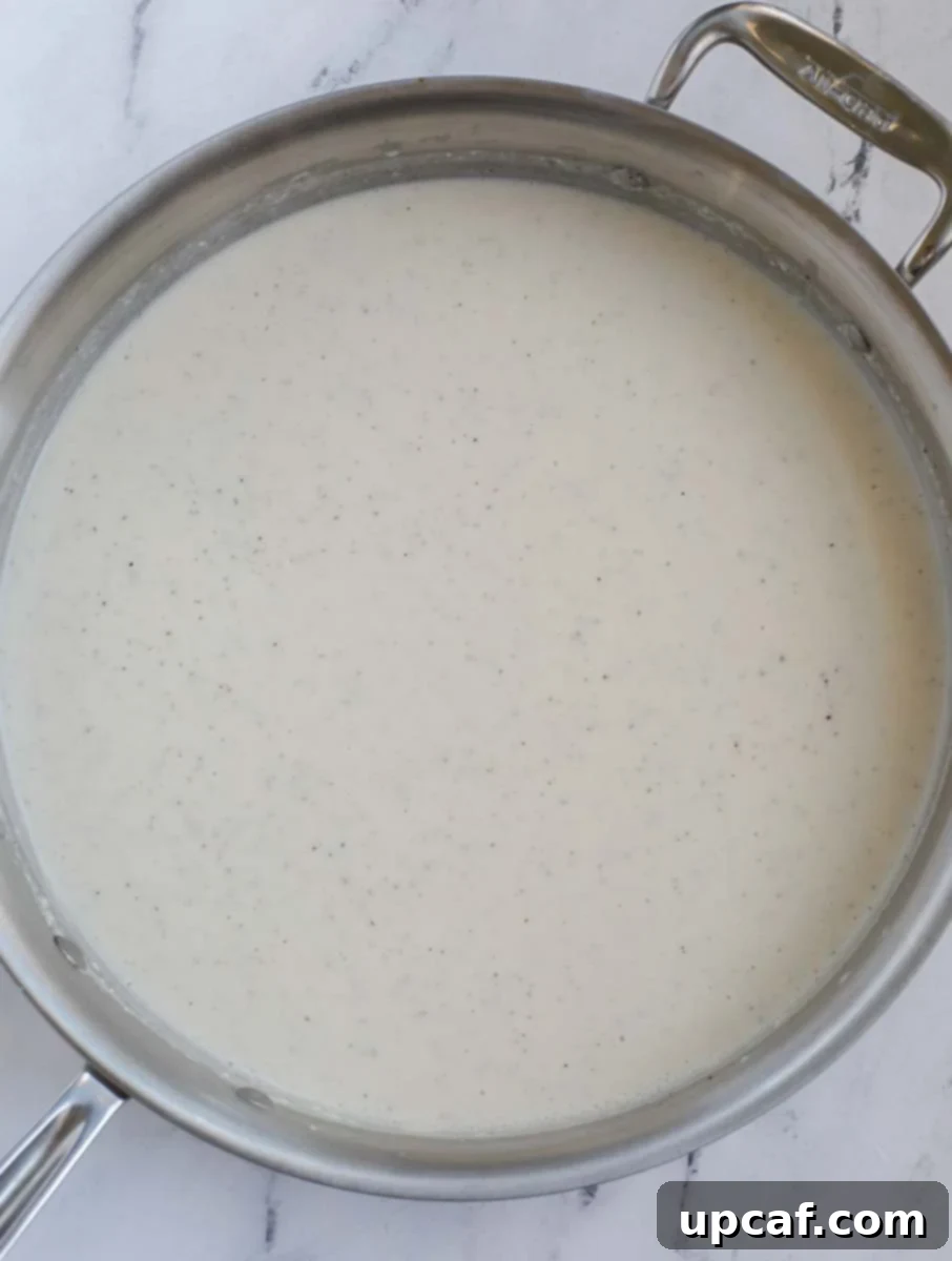 A large silver skillet on a marble counter holding a smooth, creamy casserole sauce.