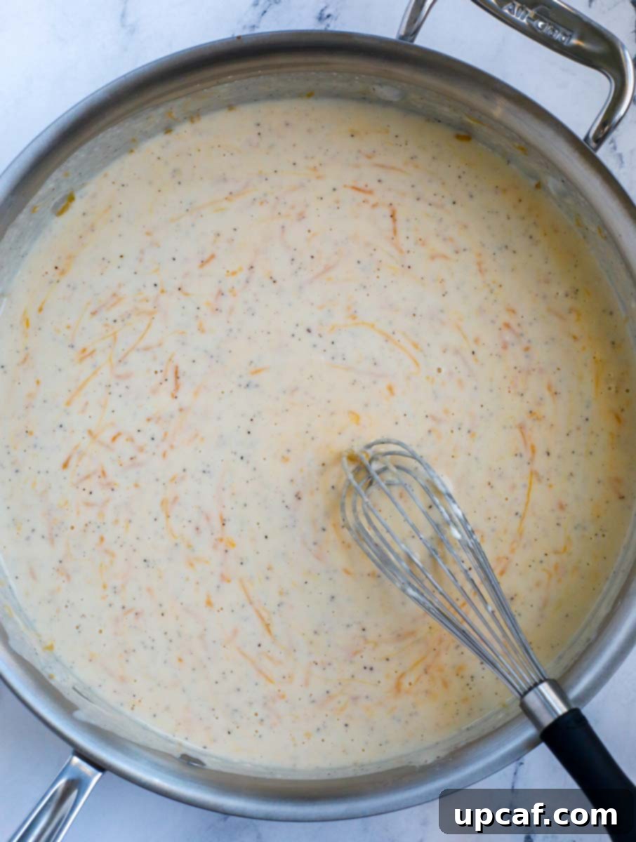 A silver skillet showcasing a creamy, cheesy casserole sauce with a wire whisk on the right side.