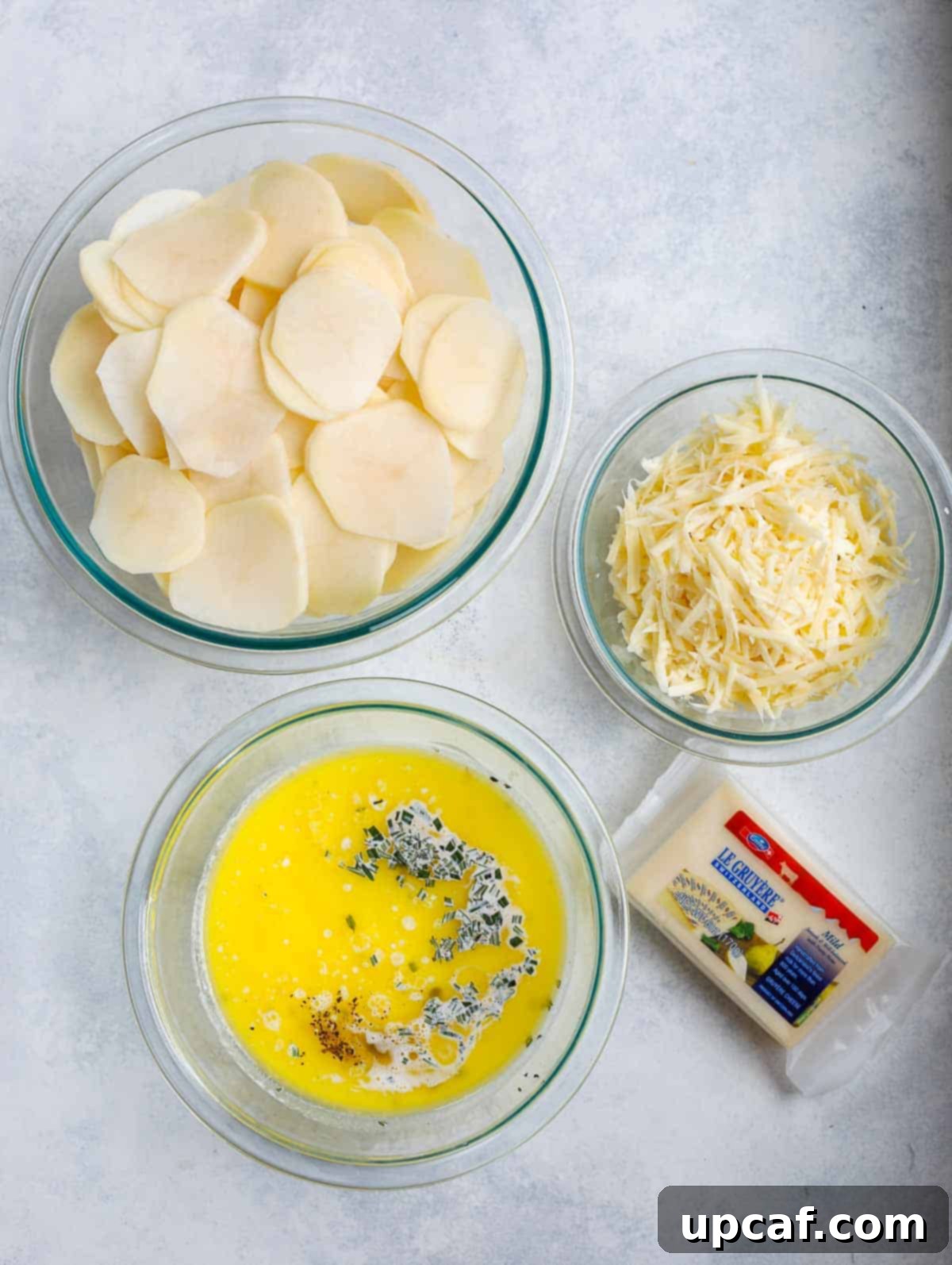 A top-down view of the fresh ingredients laid out for making potatoes au gratin, including potatoes, cheeses, cream, and herbs.