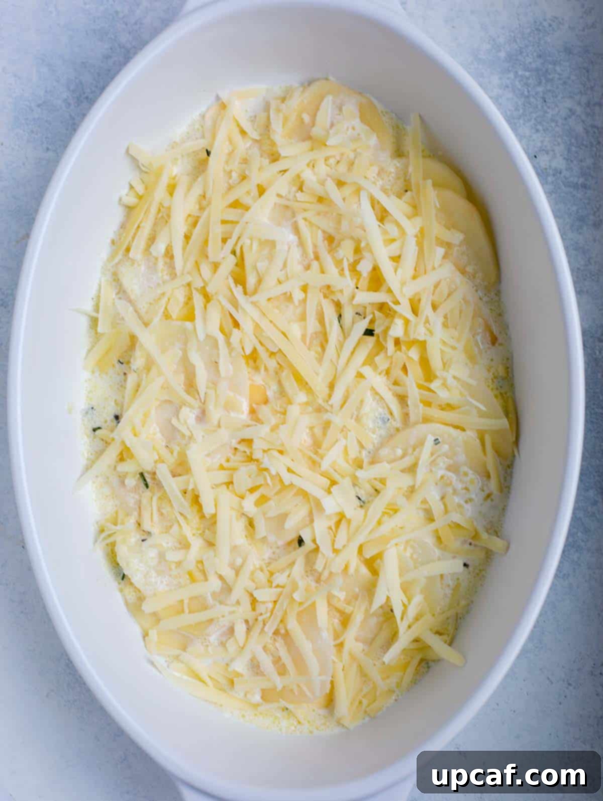 A close-up of the partially layered au gratin potatoes, showing the cream and cheese between potato slices.