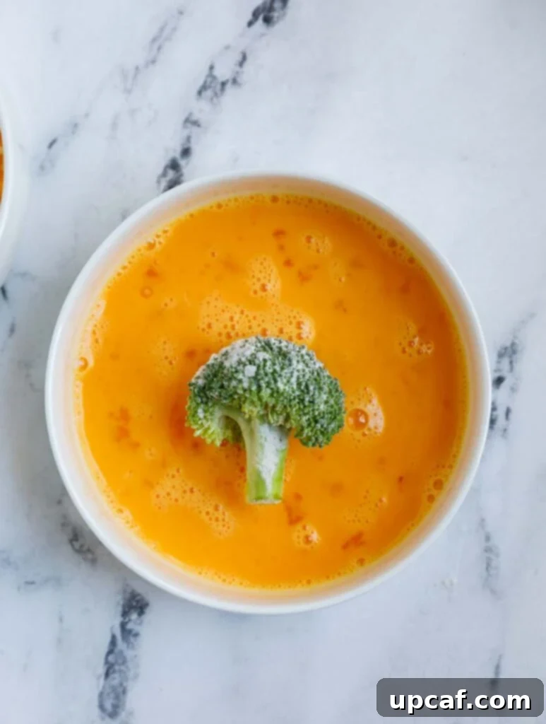 broccoli in a bowl of egg wash.