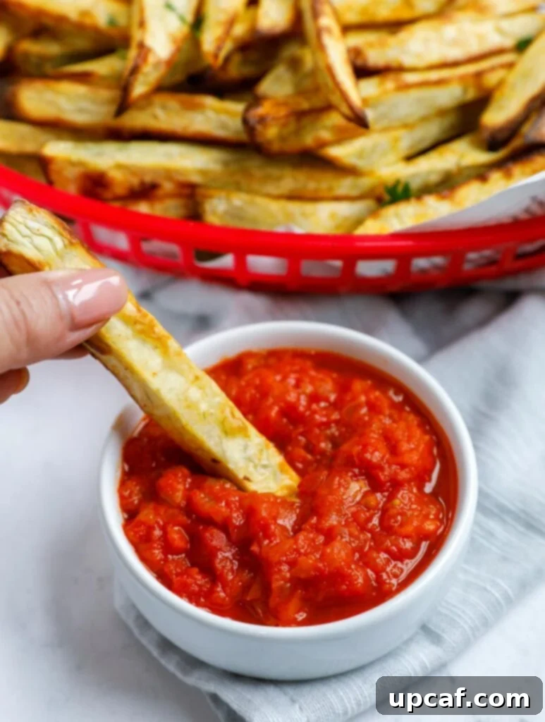Hand dipping a sweet potato fry into tomato sauce.