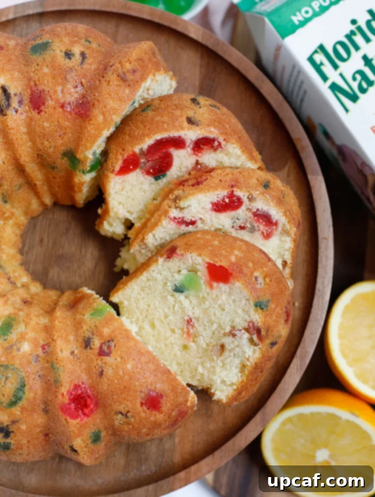Zesty Holiday Fruitcake 21 A beautifully sliced orange fruit cake arranged on a rustic wooden plate, ready to be served and enjoyed by guests.