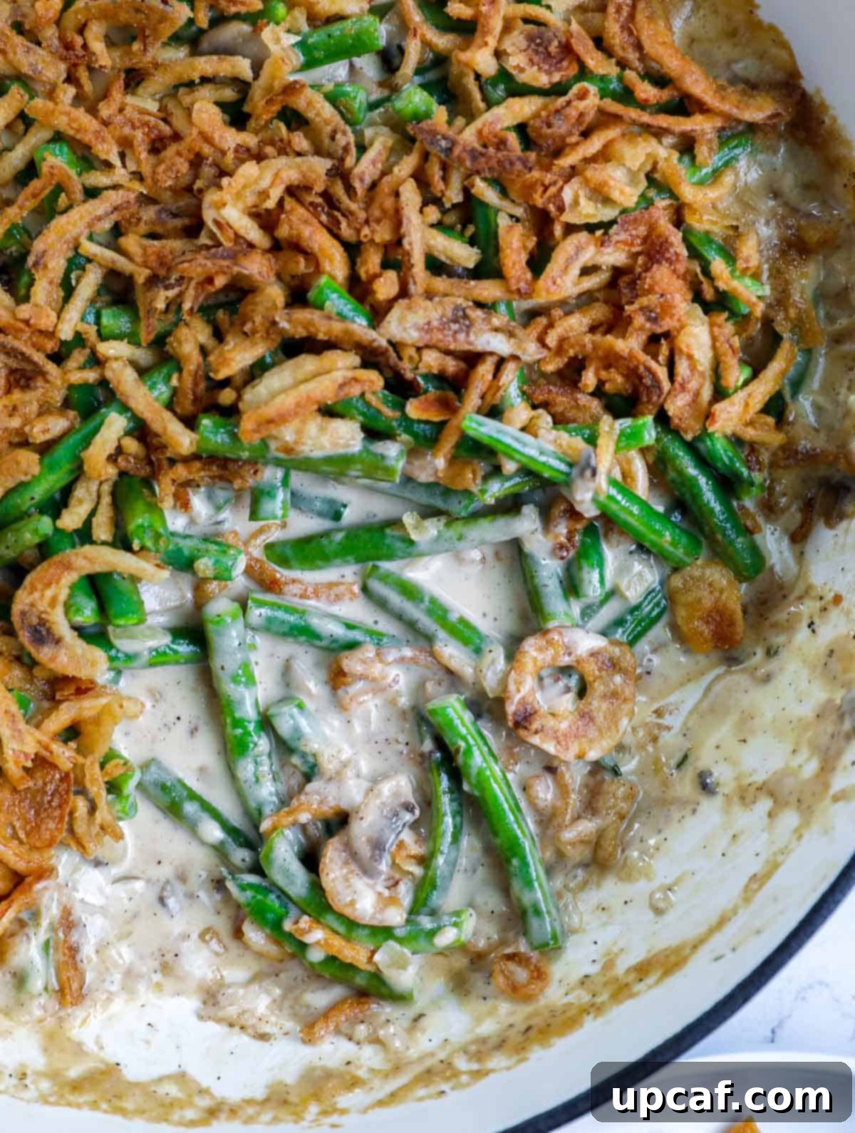 Ultimate Homestyle Green Bean Casserole 2 A serving of homemade green bean casserole with a portion removed, showcasing its creamy texture and crispy onion topping.