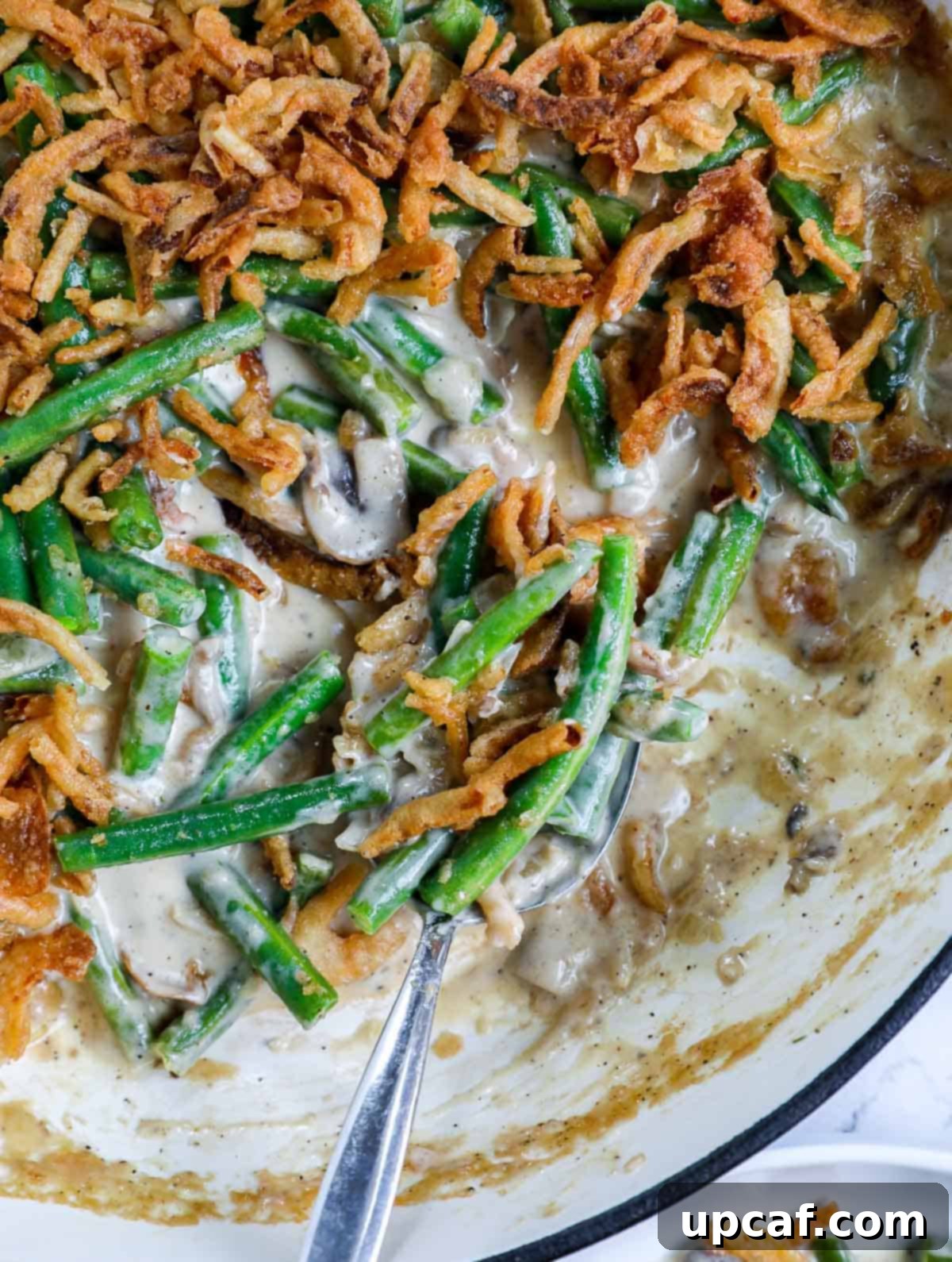 Ultimate Homestyle Green Bean Casserole 9 A serving spoon dipped into the homemade green bean casserole, showing its rich texture and topping.