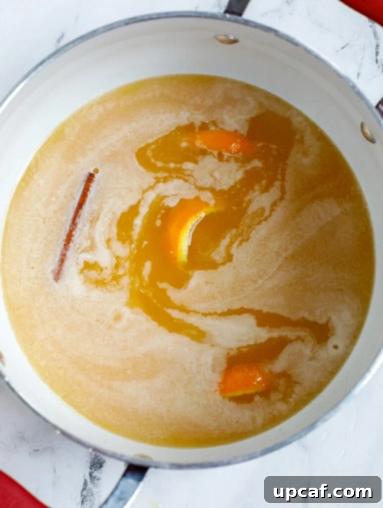 Orange juice, orange peel, sugar, and a cinnamon stick simmering gently in a saucepan on the stovetop.
