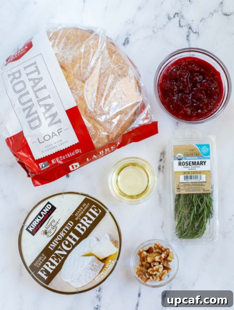 Cranberry Brie Bread Bake 3 A vibrant flat lay of ingredients for a baked brie bread bowl, including a boule loaf, a wheel of brie, cranberry sauce, olive oil, fresh rosemary, and walnuts.