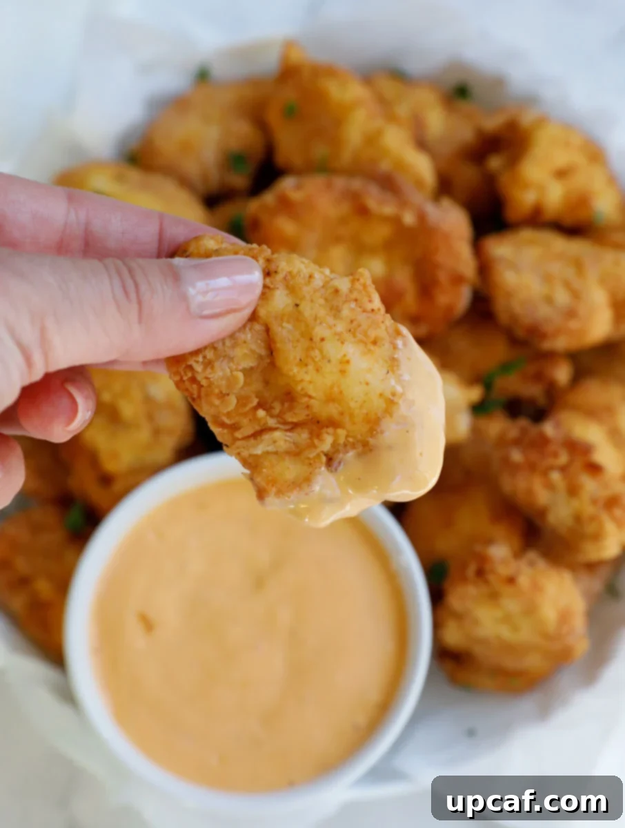 Female hand holding a piece of chicken nuggets dipped in sauce.
