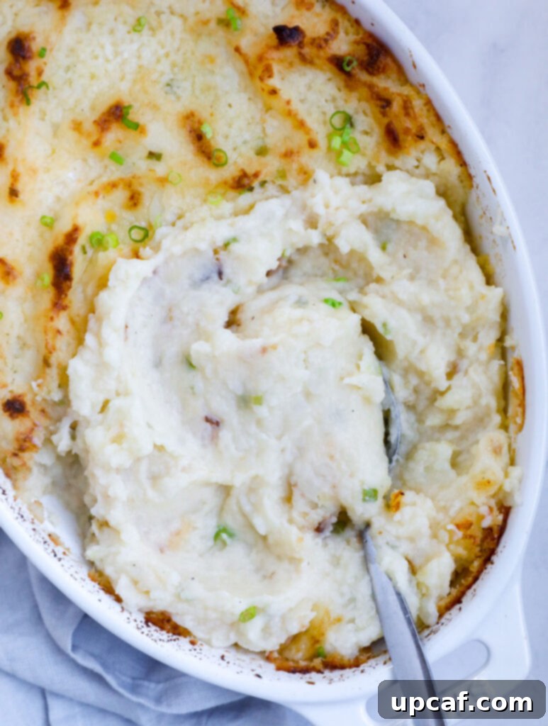 A close-up, top-down view of a serving dish filled with creamy roasted garlic mashed potatoes, garnished with fresh herbs.