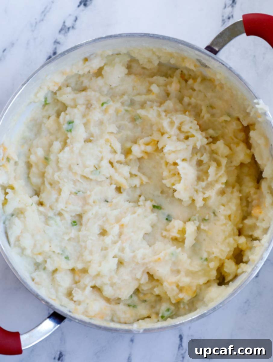 Close-up of creamy mashed potatoes being stirred in a pot, showing their smooth consistency.