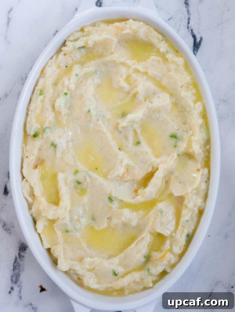 Mashed potatoes in a baking dish, topped with melted butter, just before baking.