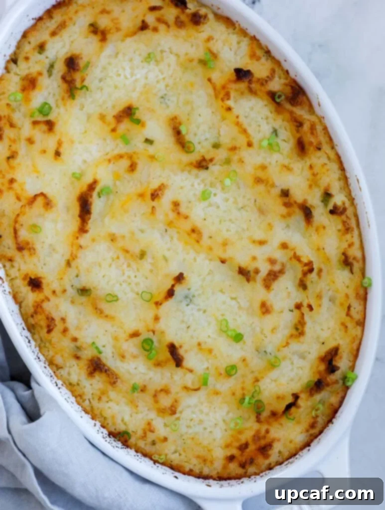 A top-down shot of roasted garlic mashed potatoes in a ceramic baking dish, perfectly golden brown and garnished with fresh chives.