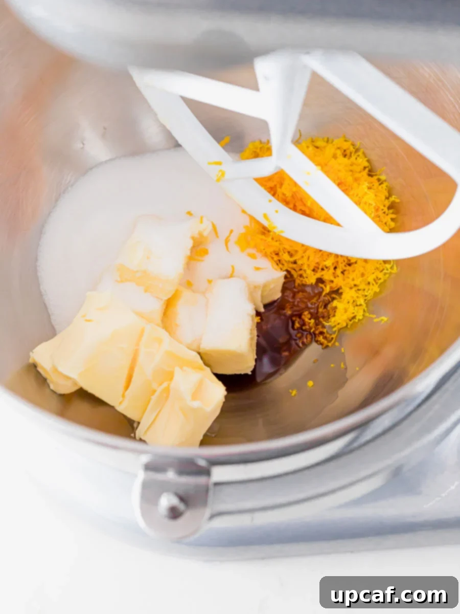 Close-up of butter, sugar, vanilla, and orange zest mixing in a stand mixer bowl, becoming light and fluffy.