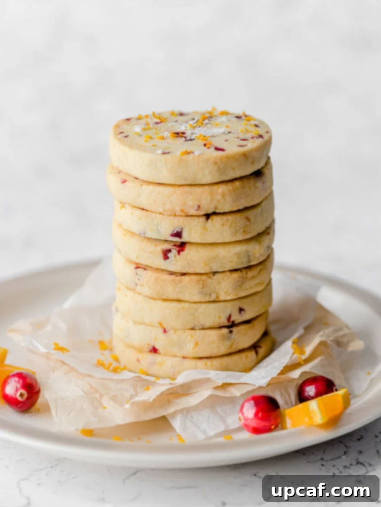 A tall and inviting stack of perfectly baked cranberry orange shortbread cookies, showcasing their uniform shape and delightful speckles, ready to be enjoyed.