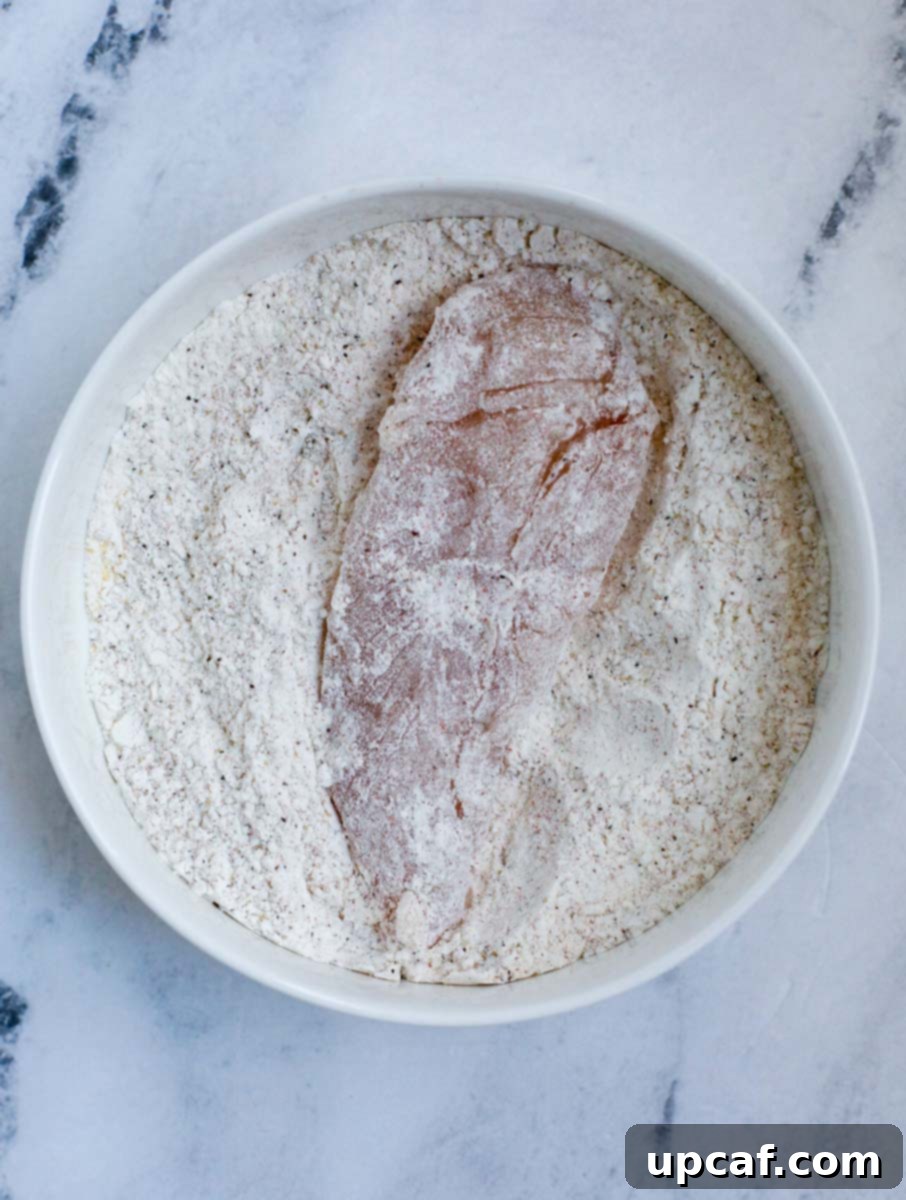 Chicken tender being coated in a seasoned flour mixture.