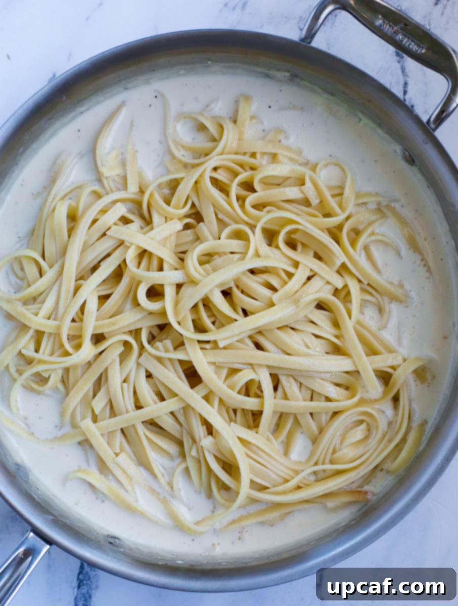 Cooked pasta being added to the creamy sauce in the skillet.