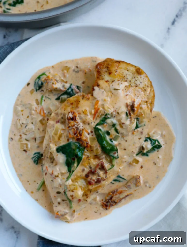 A piece of creamy Tuscan chicken breast served on a white plate with sauce.