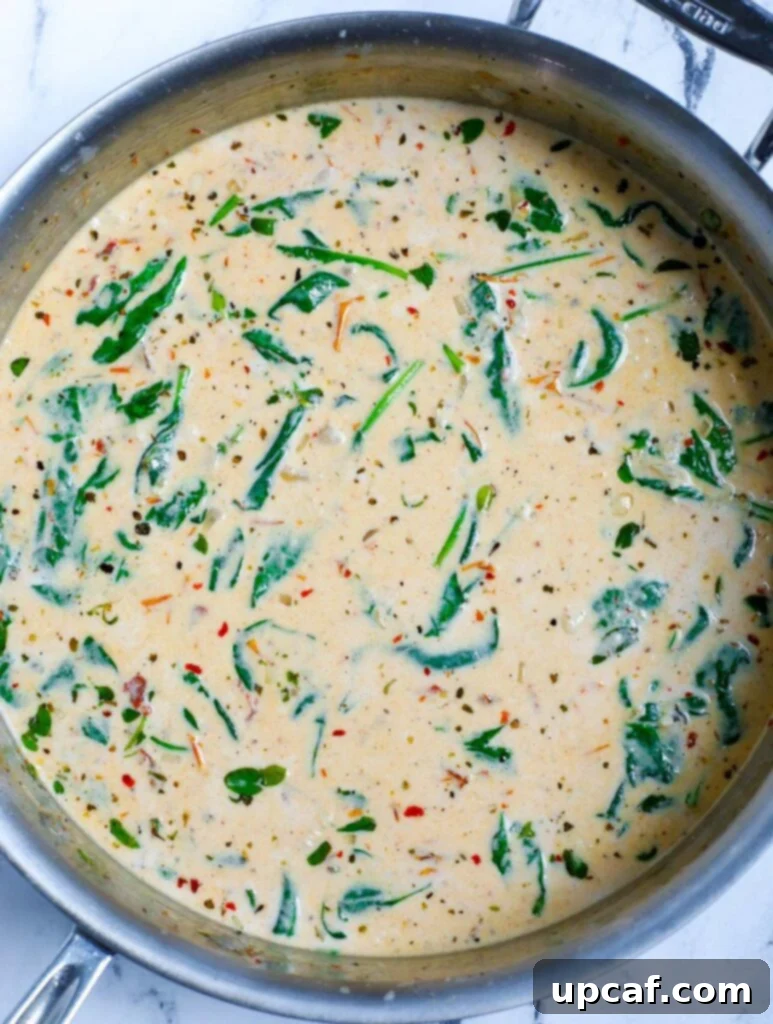 More spinach being added to the creamy sauce in the skillet.