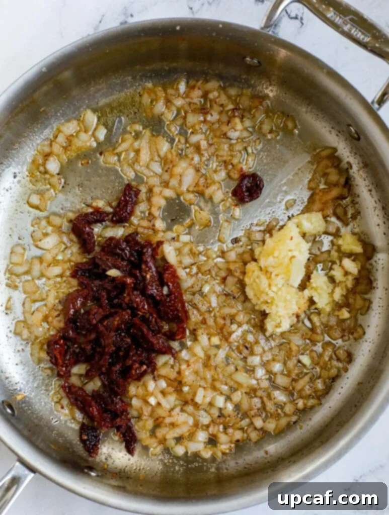 Top down view of sautéed onions, garlic, and sun-dried tomatoes mingling in the pan.