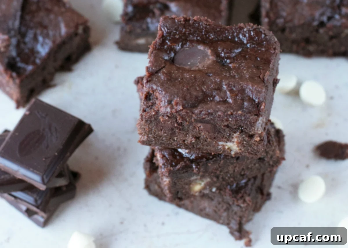Stacks of cut triple chocolate brownies on parchment paper with chips and chunks of chocolate