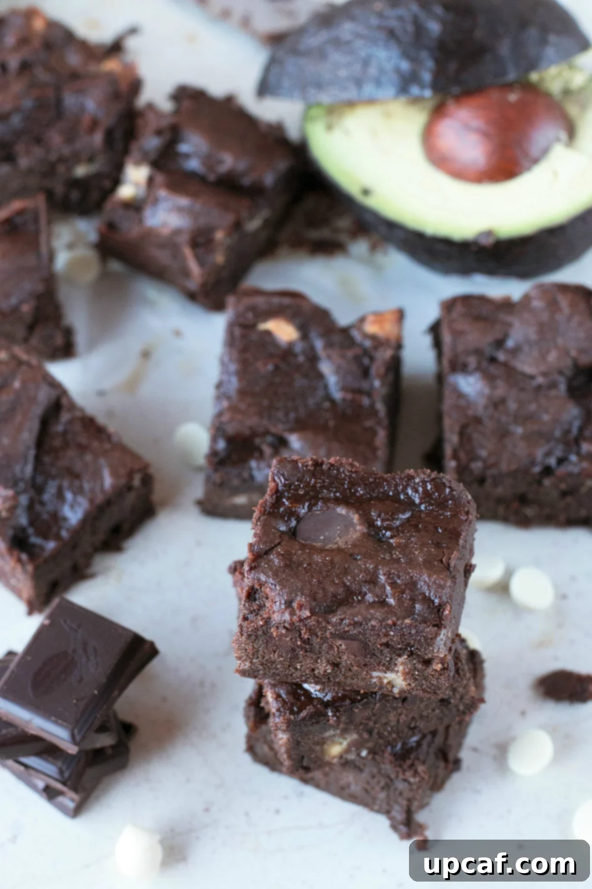 Overhead picture of a gluten-free dessert, brownies, stacked on parchment paper with avocado and chocolate chips in background