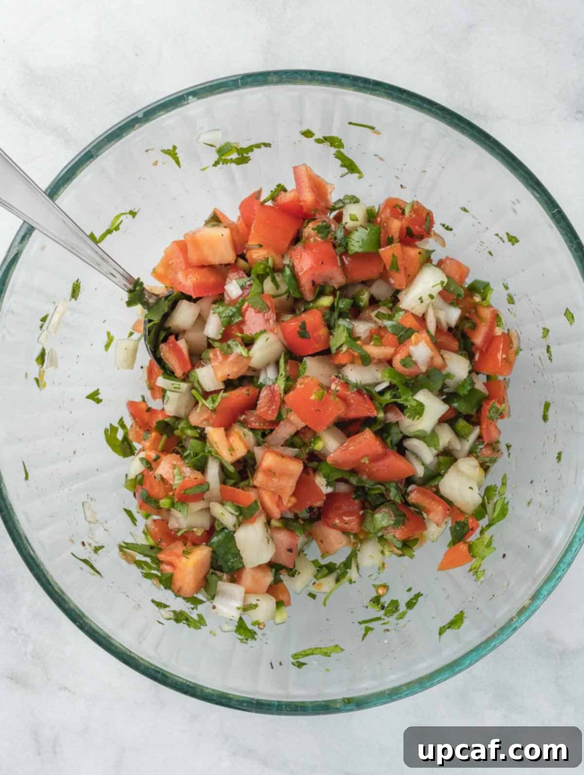 pico de gallo in a clear bowl after mixing ingredients.