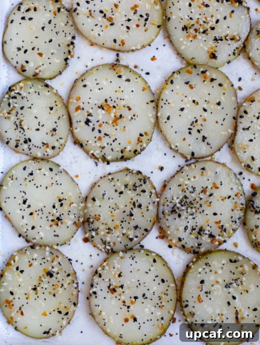 Everything Bagel Potato Crisps 5 Overhead view of seasoned potato slices arranged in a single layer on a parchment-lined baking sheet.
