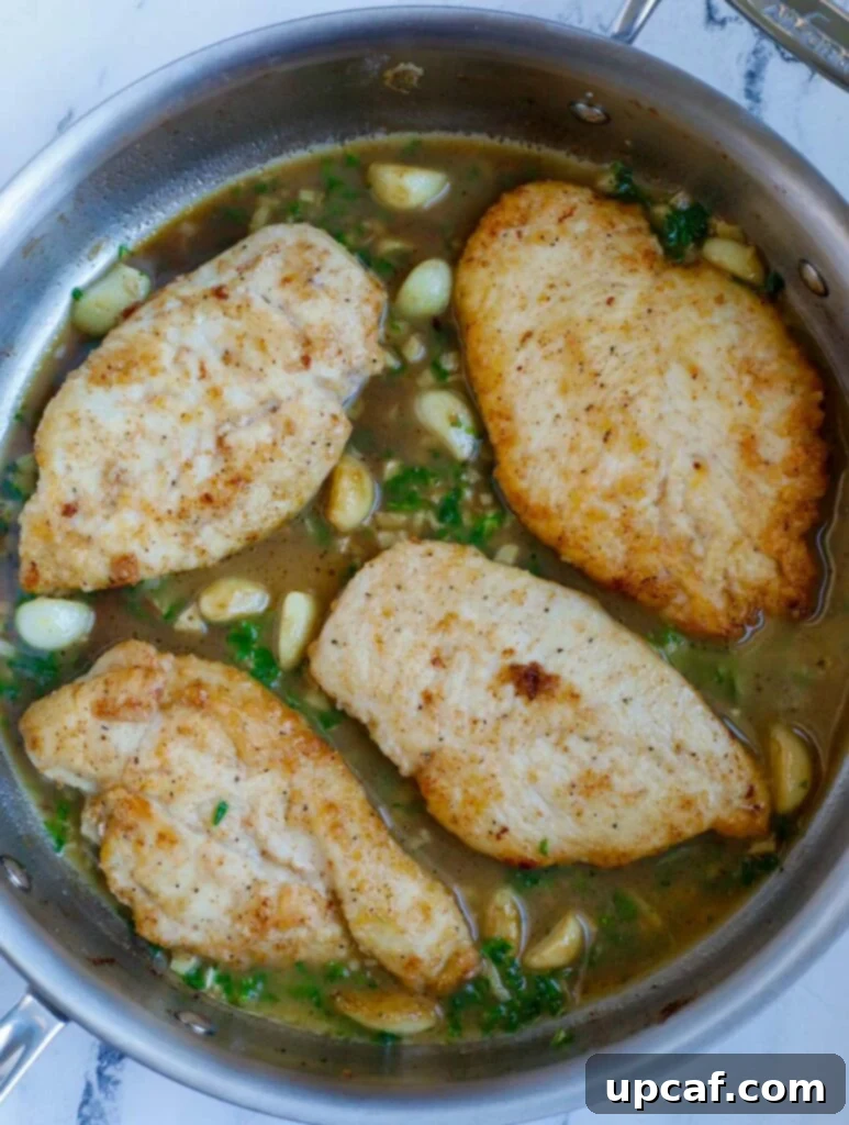 Top down view of a skillet filled with lemon and garlic chicken, glistening with sauce and garnished with parsley.