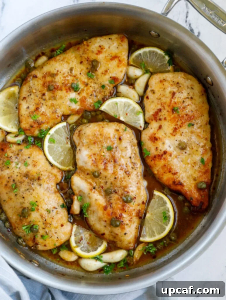 Top down view of lemon chicken piccata in a pot, garnished with fresh lemon slices and parsley.
