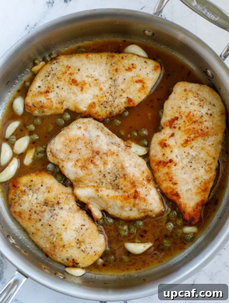 Lemon chicken piccata pieces returned to the pan, coated in the simmering, vibrant lemon-caper sauce.