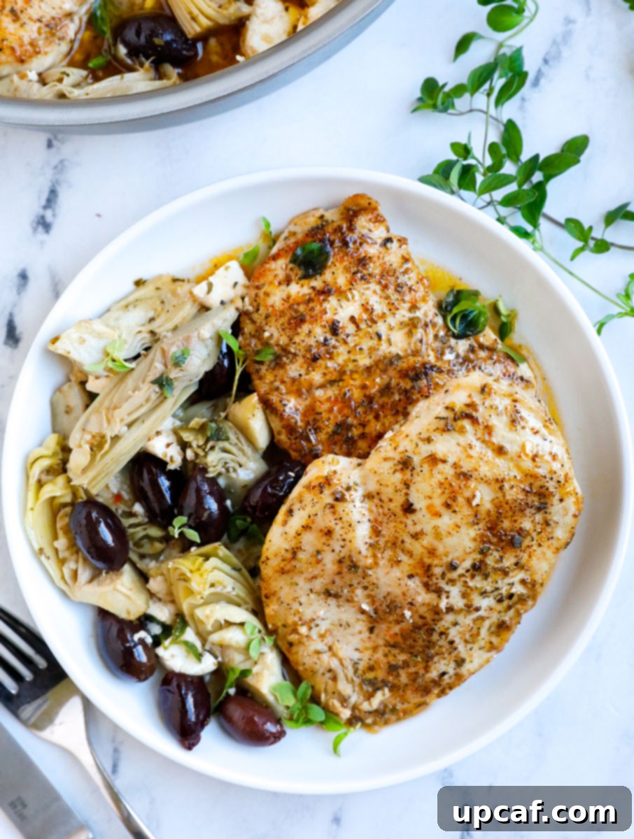 Greek chicken breasts served on a white plate with sauce, olives, and feta.