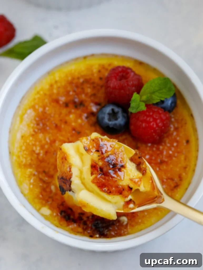 Effortless Crème Brûlée 2 A spoon breaking into the crispy caramel topping of a homemade crème brûlée, revealing the creamy custard beneath.