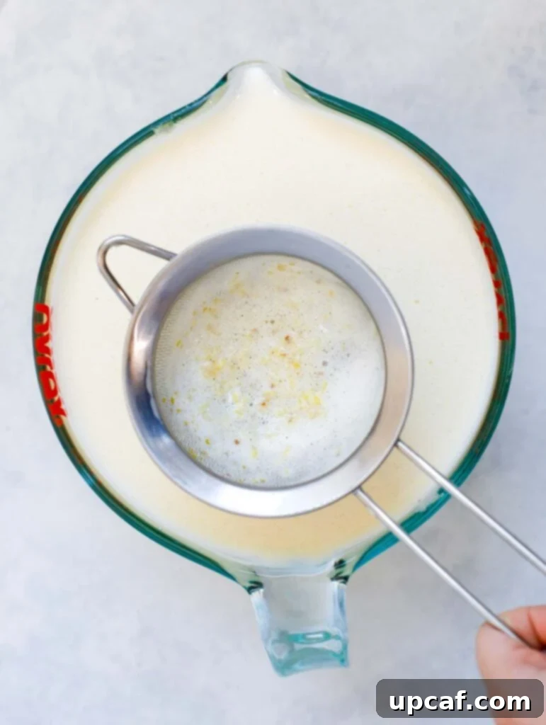 Effortless Crème Brûlée 7 A fine-mesh sieve being used to strain the cooked custard mixture into a measuring cup for a silky smooth finish.