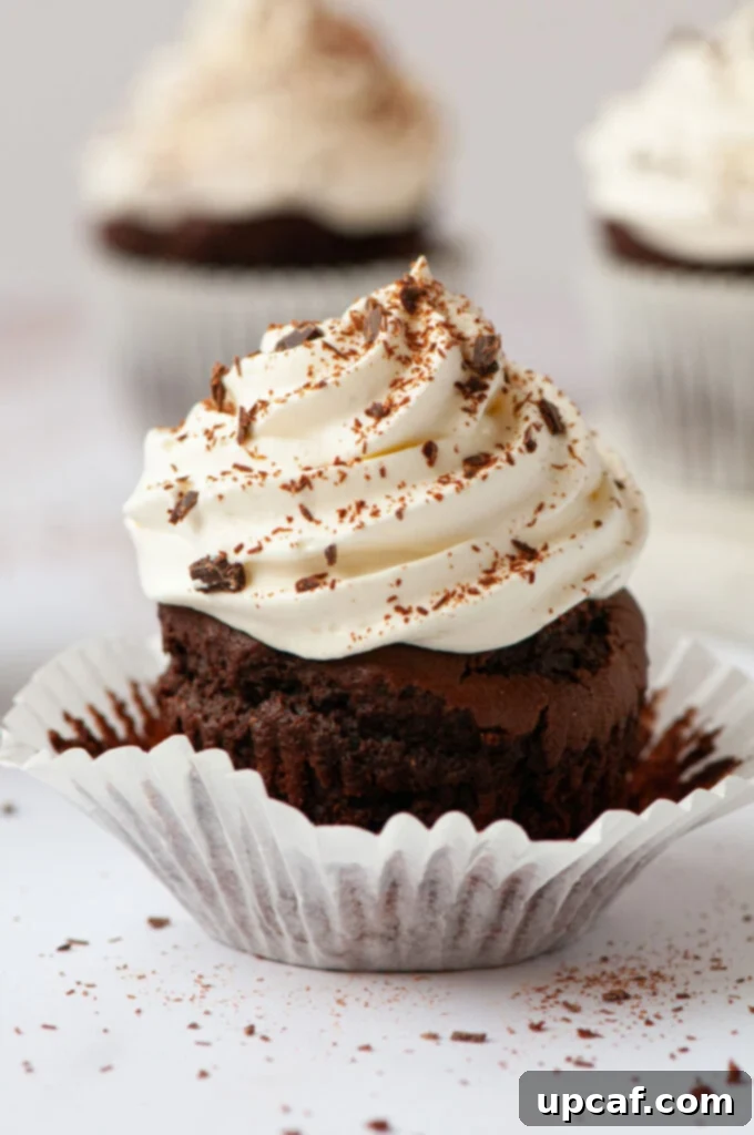 Fudgy Vegan Chocolate Perfection 8 A vegan chocolate cupcake with its wrapper partially peeled down, revealing its rich, moist interior and delicious whipped frosting.