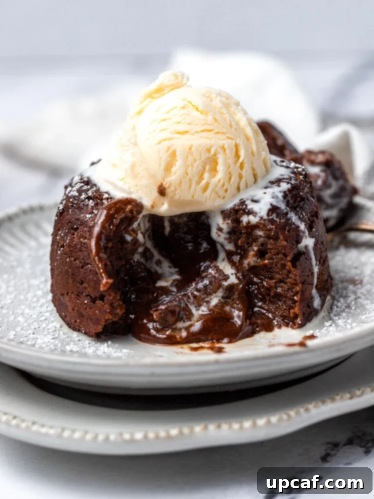 A molten chocolate lava cake cut open, revealing its gooey center, served with a scoop of vanilla ice cream on top.