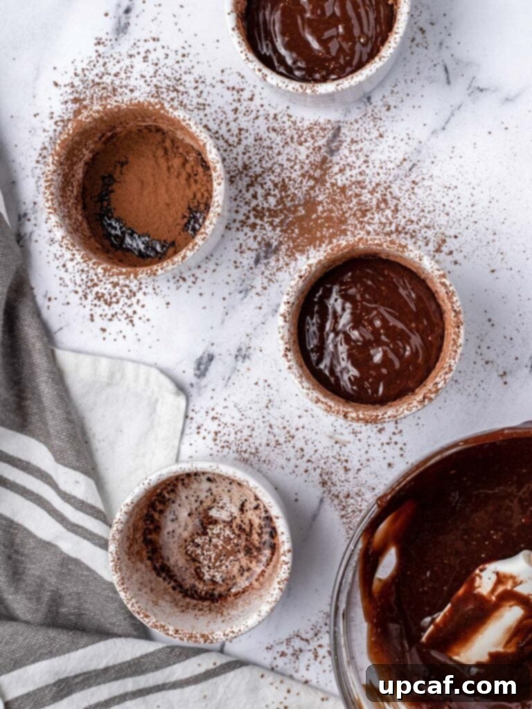 Four prepared ramekins, two of which are filled with chocolate lava cake batter, ready for baking.